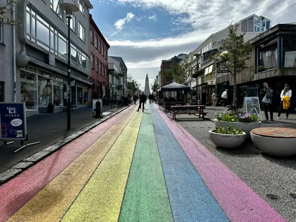 In Regenbogenfarben bemalte Straße, die auf einen Kirchturm zuläuft